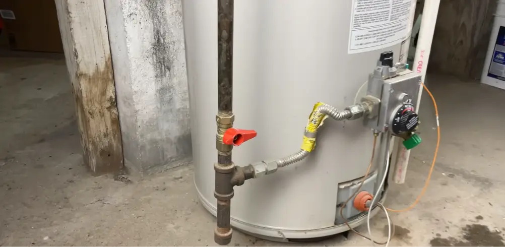 Gas water heater with a red handled gas shutoff valve and thermostat in a basement