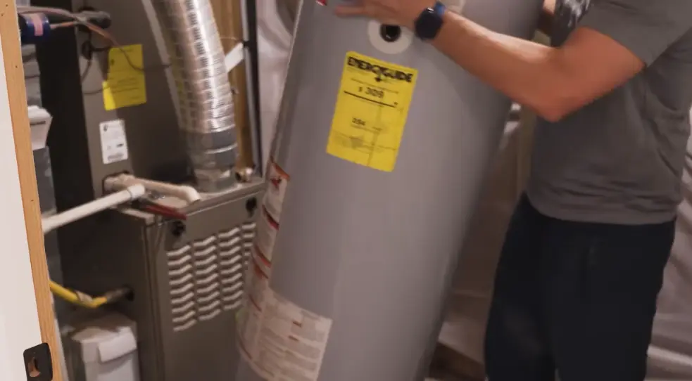 Technician lifting a new tank water heater into place next to a furnace