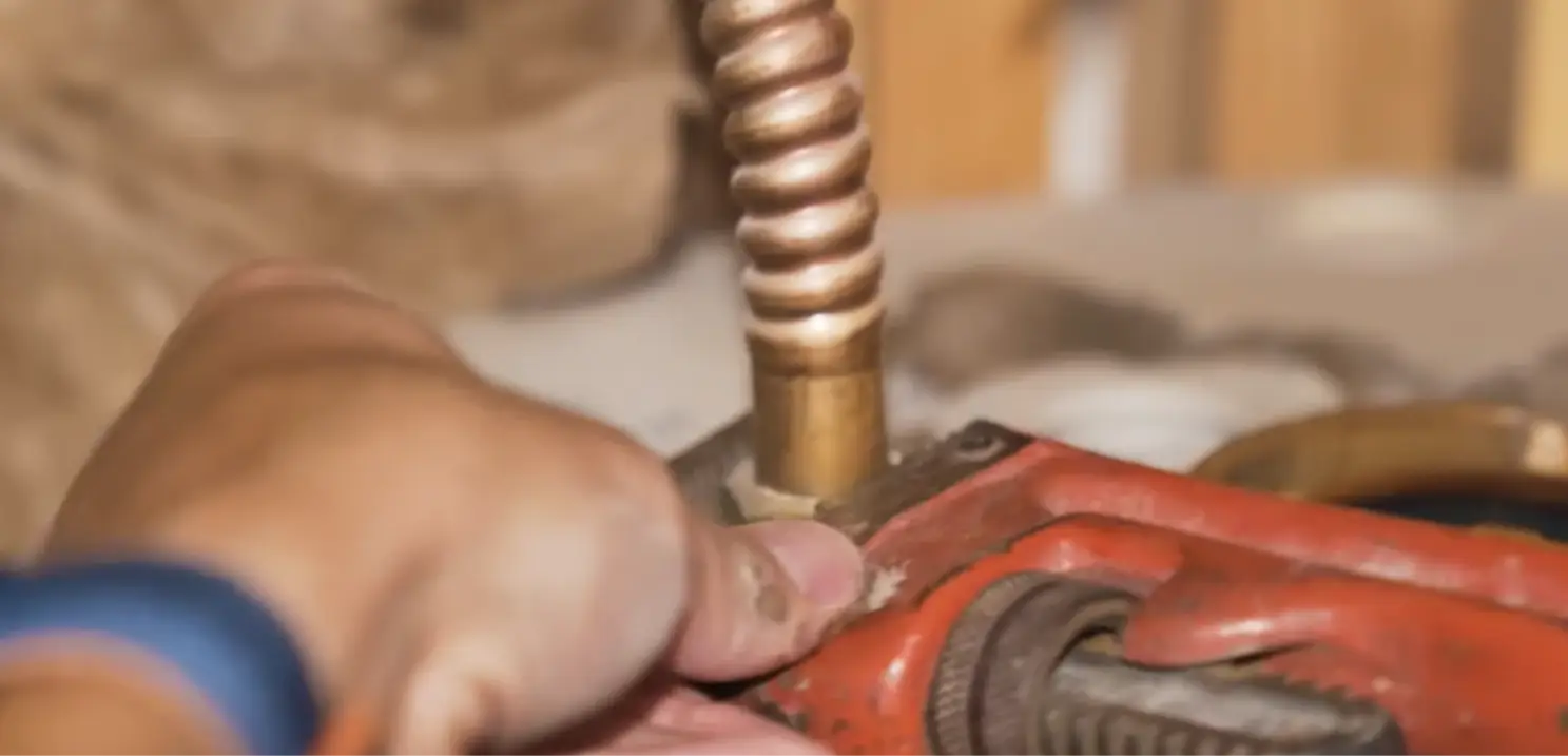 Plumber tightening a copper gas connector on a water heater with a pipe wrench