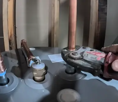 Press tool crimping a copper fitting on top of a water heater